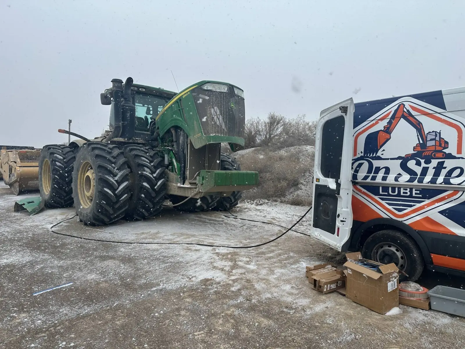 On Site Lube van with its back doors open, servicing a John Deere 9560R tractor in the snow