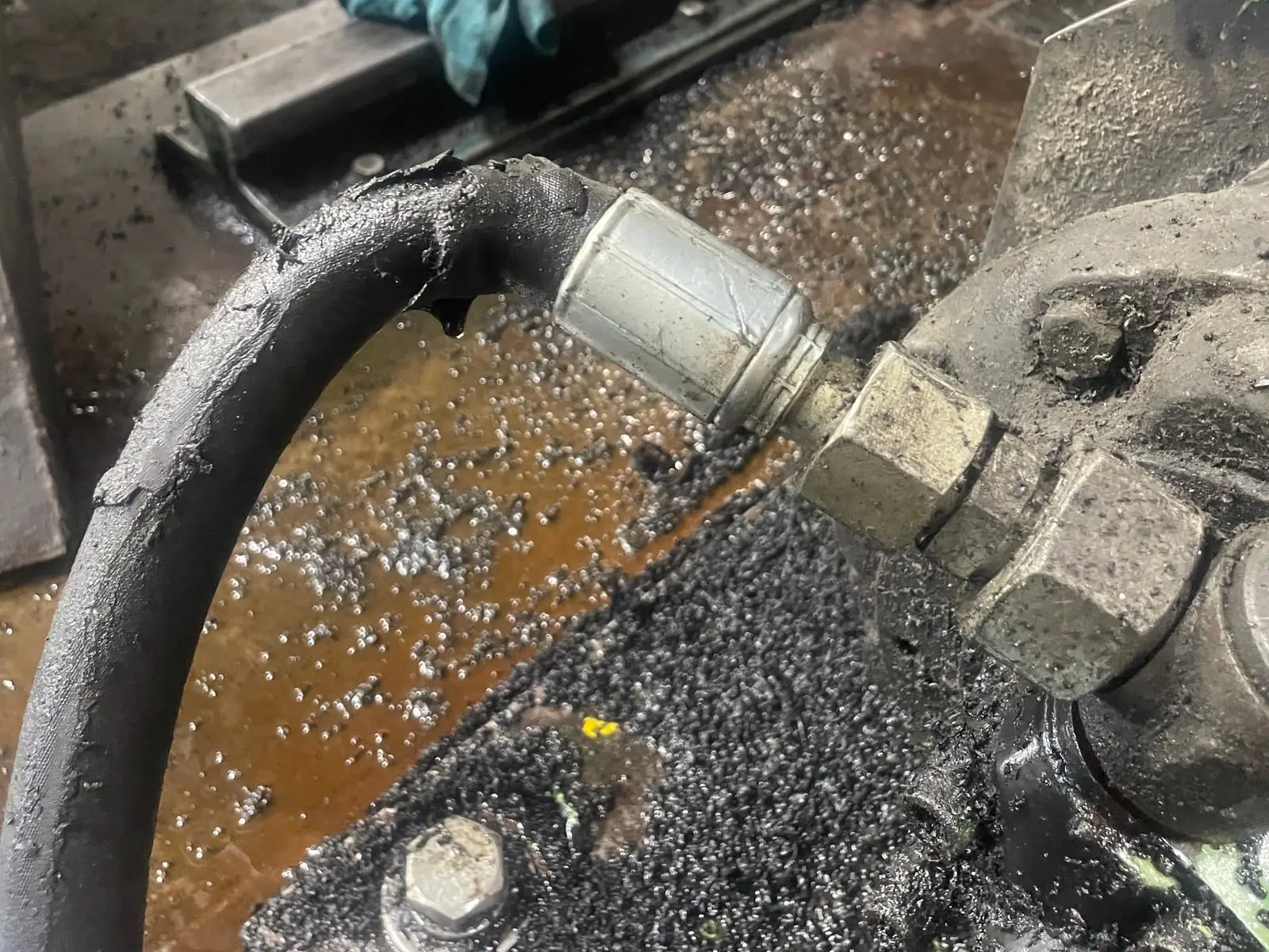 Hydraulic hose with its outer cover torn away at the fitting and oil dripping, a hose that will blow if it isn't replaced