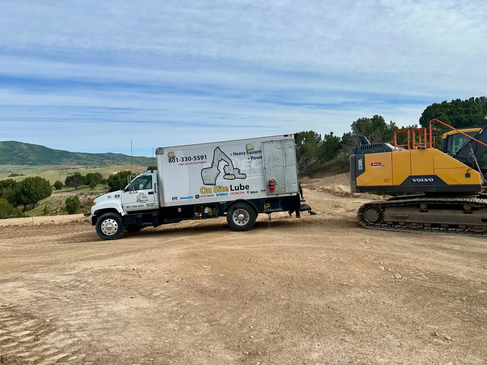 On Site Lube service truck parked beside a Volvo excavator on a hillside jobsite