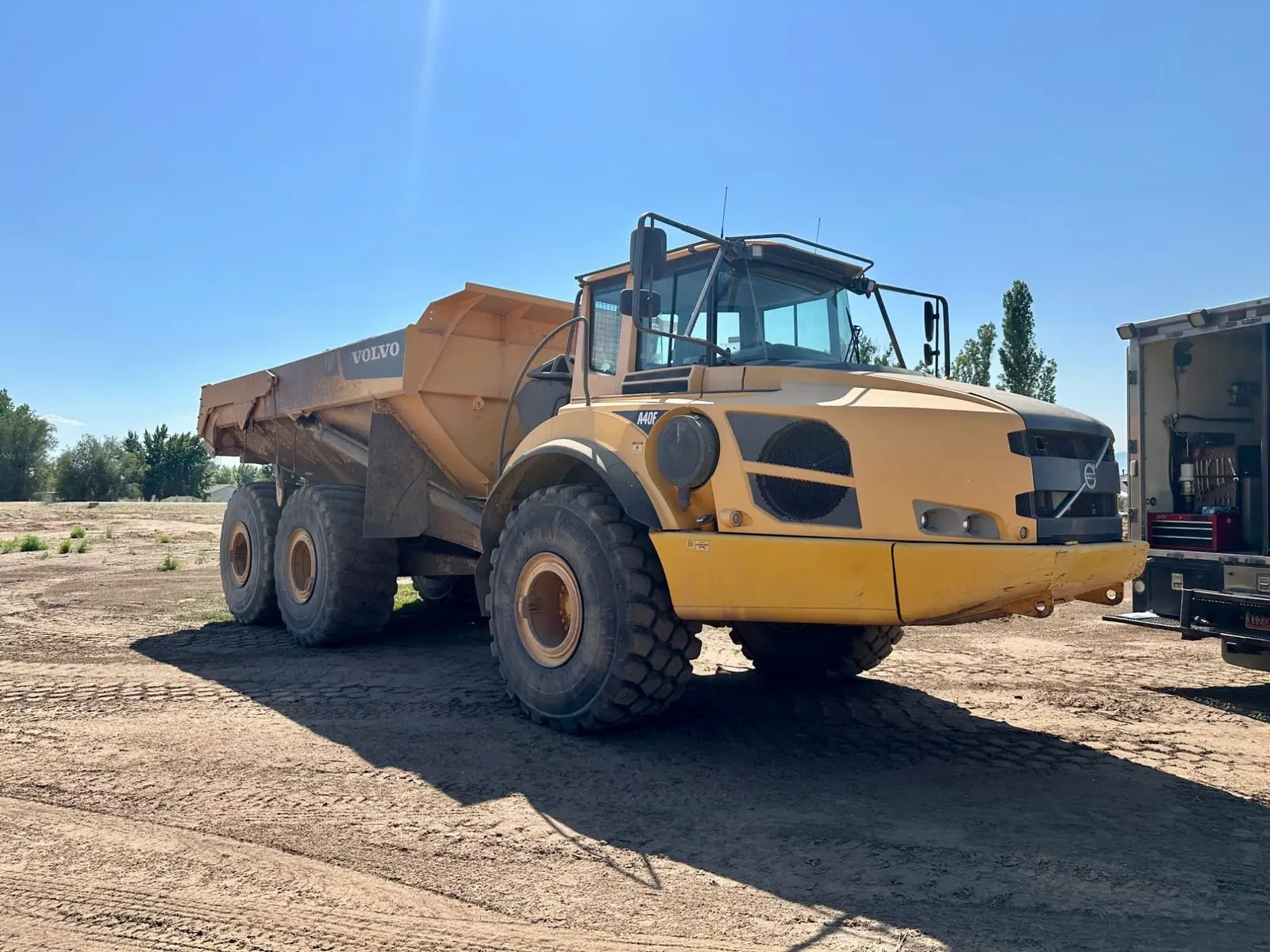 Volvo A40F articulated haul truck parked on a dirt jobsite, with a service truck alongside
